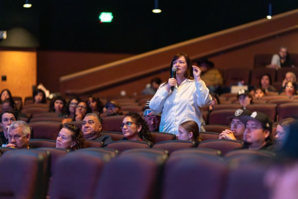 A woman stands in a packed theater audience and speaks into a microphone during a Q&A at a People of the West screening.