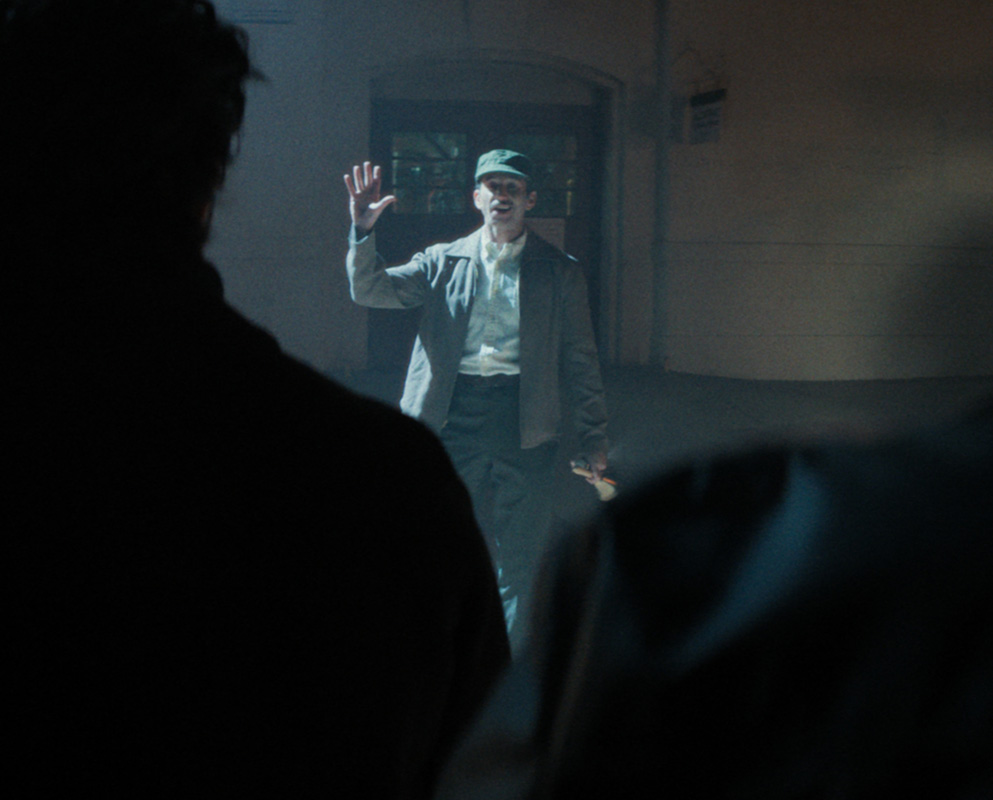 A Native man in a work cap raises his hand as he faces silhouetted figures on a dark street at night, in a scene from People of the West.