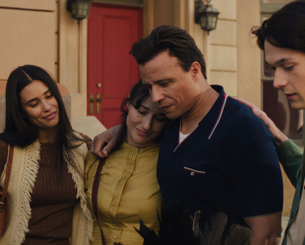 A Native family in 1950s clothing shares a tearful embrace outside a building with a red door, in a scene from People of the West.