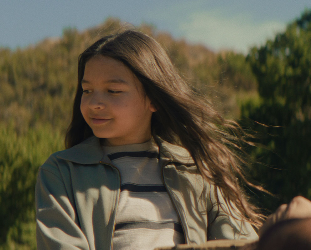 A young Native girl with long, windblown hair smiles softly on a sunlit hillside in a scene from People of the West.