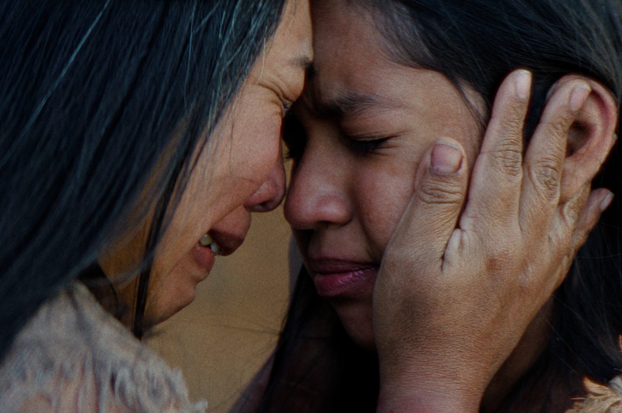 Two Native women press their foreheads together in tears as the older woman cups the younger woman’s face, in a scene from People of the West.