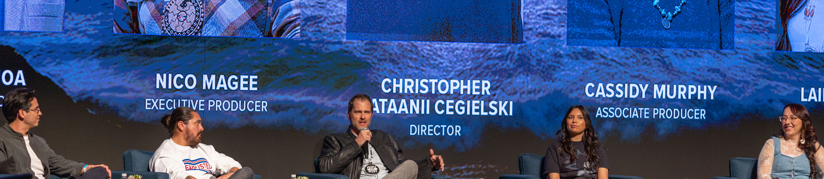 Five panelists sit on stage at a People of the West event, in front of a large screen listing the series’ creator, producers, and director.