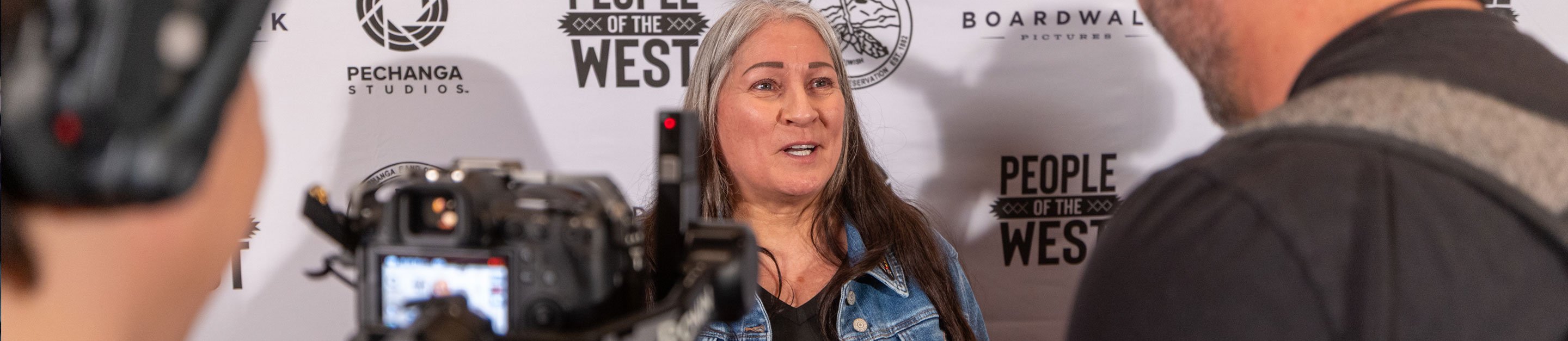 A woman with long gray hair is interviewed on camera in front of a People of the West backdrop with Pechanga Studios and Boardwalk Pictures logos.