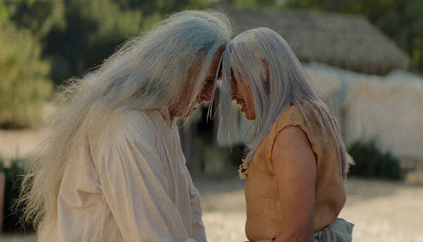 Two Native elders with long white hair touch foreheads in a village of thatched dwellings, in a scene from People of the West.