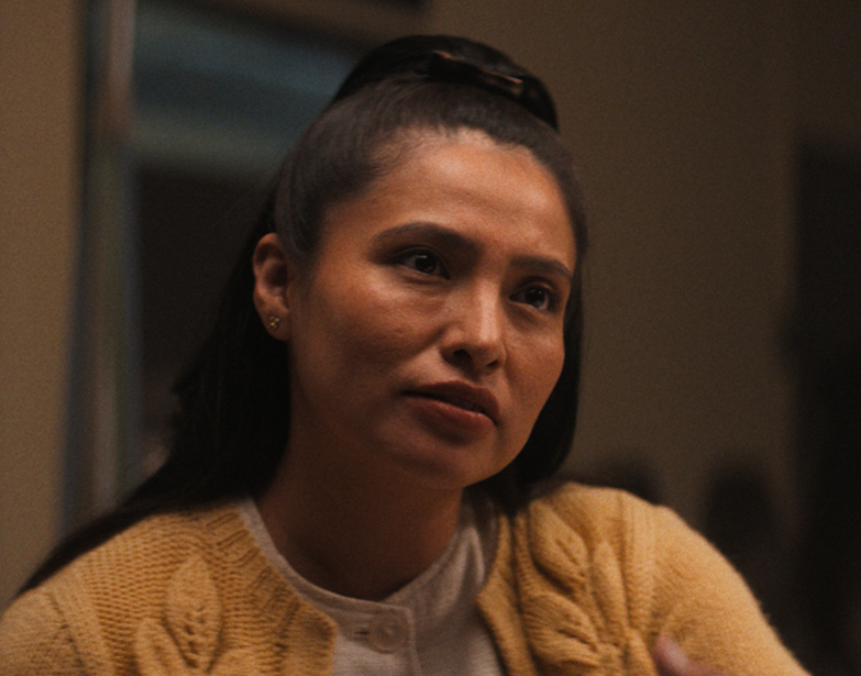 A Native woman in a mustard cardigan speaks with a worried expression, in a scene from People of the West.