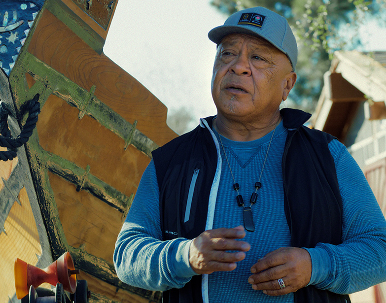 Tribal Elder Reggie Pagaling in a cap and vest speaks in People of the West.