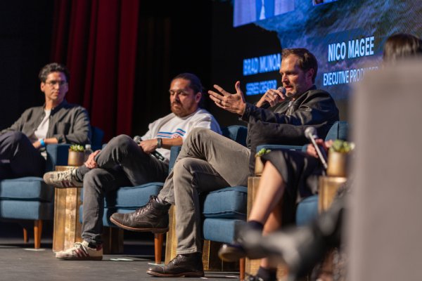 Three filmmakers sit in armchairs on stage during a People of the West panel discussion as one in a leather jacket speaks into a microphone, with a screen behind them naming the series’ creator and executive producer.
