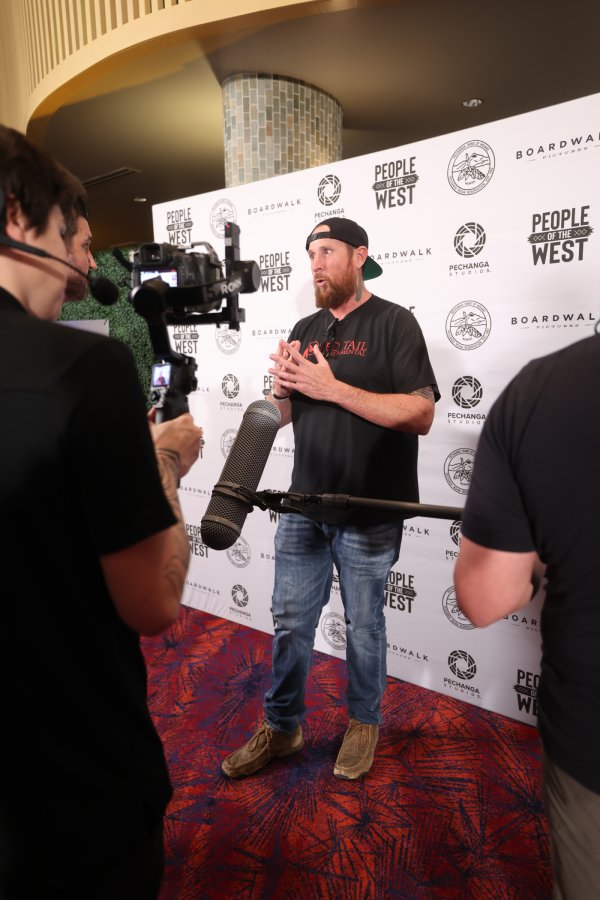 A bearded man in a backward cap is interviewed on camera in front of a People of the West backdrop with Pechanga Studios and Boardwalk Pictures logos.