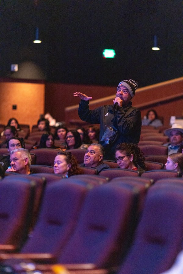 A man in a knit beanie stands in a theater audience and speaks into a microphone during a Q&A at a People of the West screening.